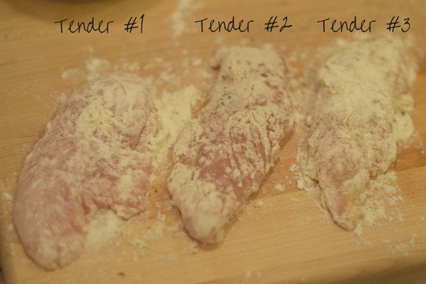 3 raw chicken tenders on a wood surface, all three are dredged