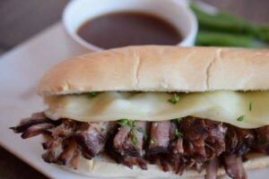 french dip with beef and melted provolone cheese on a hoagie bun with bowl of au jus in background